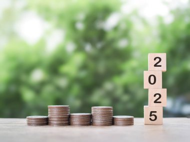 2025 numaralı tahta bloklar ve bir yığın bozuk para. 2025 yılında para, finans, yatırım ve işletme tasarruf kavramı büyüyor.