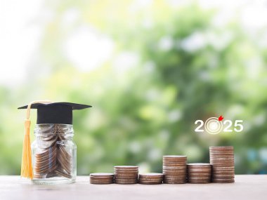 Mezuniyet şapkası ve bozuk paralarla dolu cam bir şişe. 2025 yılında eğitim, öğrenci kredisi, burs, öğrenim ücreti için para biriktirme kavramı