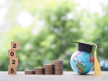 Mezuniyet şapkası ve bozuk paralarla dolu bir dünya küresi. 2025 yılında eğitim, öğrenci kredisi, burs, öğrenim ücreti için para biriktirme kavramı