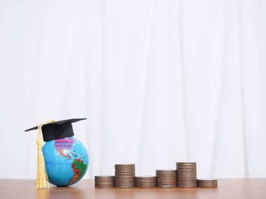 Mezuniyet şapkası ve bozuk paralarla dolu bir dünya küresi. Eğitim için para biriktirme kavramı, öğrenci kredisi, burs, gelecekte öğrenim ücretleri