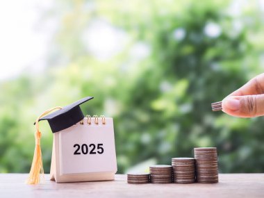 El kapama, bozuk para yığınına para koyma ve mezuniyet şapkalı 2025 masa takvimi. Eğitim, öğrenci kredisi, burs, eğitim ücretleri için para biriktirme kavramı