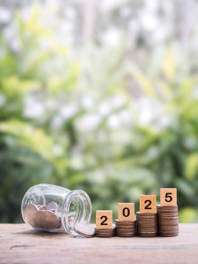 2025 numaralı tahta bloklar madeni para yığınının üzerinde. 2025 yılında para, finans, yatırım ve işletme tasarruf kavramı büyüyor.