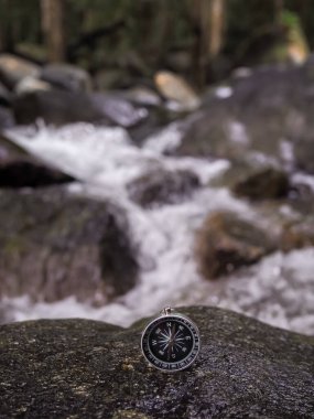 Arka planında şelale olan bir pusula. Dünya turizm günü konsepti, doğru yönleri aramak ve seyahat etmek.