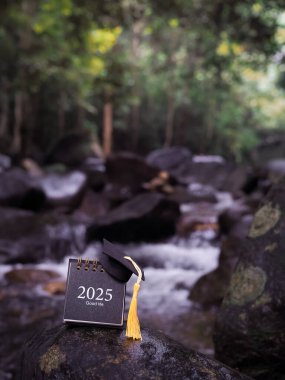 Study goals, 2025 Desk calendar with graduation hat on the rock with waterfall as background. The concept for Resolution, Goal, Action, Planning, and manage time to success graduate. clipart