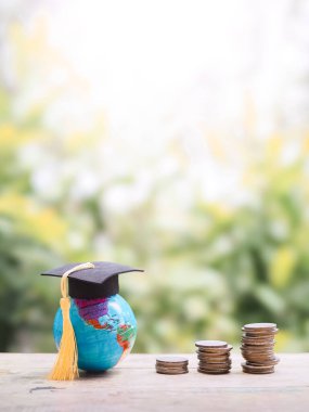 Mezuniyet şapkası ve bozuk paralarla dolu bir dünya küresi. Eğitim için para biriktirme kavramı, öğrenci kredisi, burs, gelecekte öğrenim ücretleri