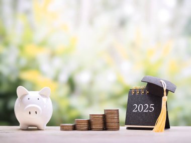 Study goals. 2025 desk calendar with graduation hat, stack of coins and piggy bank. The concept of saving money for education, student loan, scholarship, tuition fees in year 2025 clipart