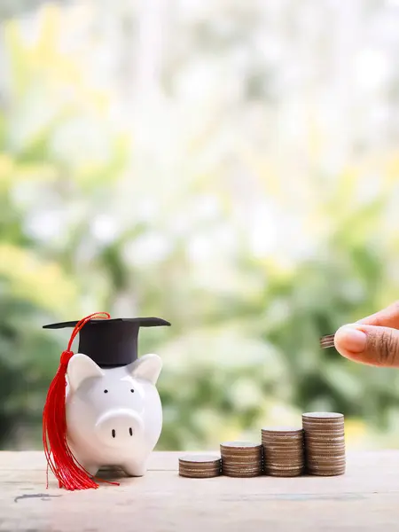 El sıkışın, bozuk para yığınına ve mezuniyet şapkalı domuz kumbarasına para atın. Eğitim için para biriktirme kavramı, öğrenci kredisi, burs, gelecekte öğrenim ücretleri