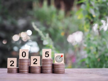 2025 numaralı tahta bloklar madeni para yığınının üzerinde. 2025 yılında para, finans, yatırım ve işletme tasarruf kavramı büyüyor.