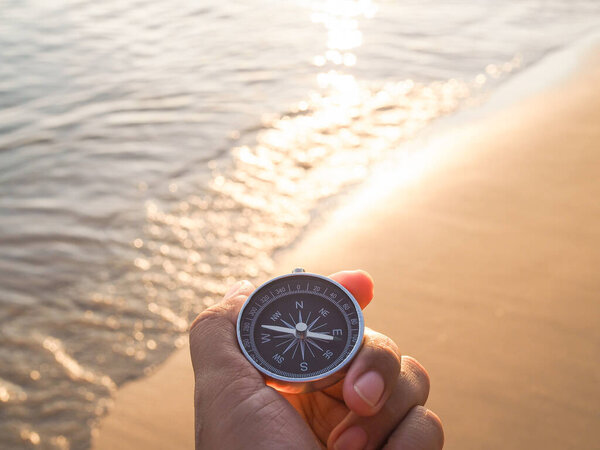 Close up hand holding compass with beach background in the sunset time