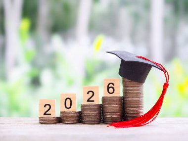 2026 numaralı tahta bloklar ve mezuniyet şapkalı bozuk paralar. 2026 yılında eğitim, öğrenci kredisi, burs, öğrenim ücreti için para biriktirme kavramı