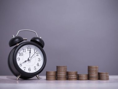 Siyah çalar saat ve bir yığın bozuk para. İş hayatına zaman ayırmak için para biriktirme kavramı.