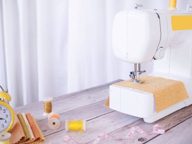 Sarı kumaşla çalışan dikiş makinesini kapatın, masaya aksesuarlar dikin, yeni kıyafetler dikin..