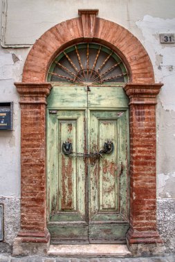 Eski yeşil kapı, duvarları soyulmuş iki kırmızı tuğla sütun arasında zincir ve asma kilit ile kapatılmış..