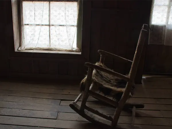 stock image Antique wooden rocking chair with straw seat inside an old wooden house.