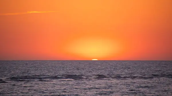 stock image Setting sun descending into ocean water with a fiery sky