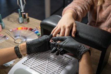 Güzellik uzmanı kadın müşterinin tırnaklarını profesyonel elektrikli çivi matkabıyla güzellik salonunda törpülüyor. Donanım manikürü.