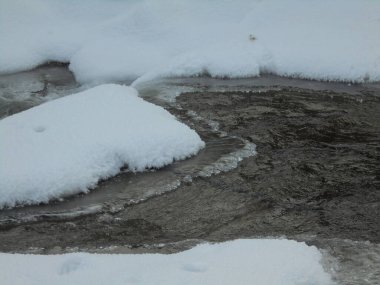 Freezing wild rive flowing through snowy nature of Czech mountains,having ice remaining on the surface