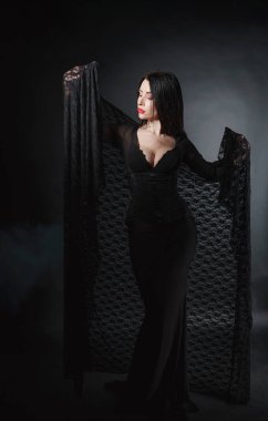 Beautiful sexy girl with a mystical look in a black bodycon dress on a black background