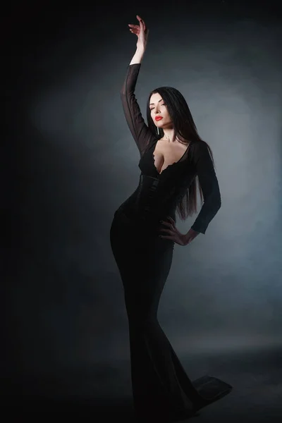 Beautiful sexy girl with a mystical look in a black bodycon dress on a black background