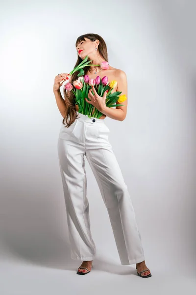 A slender girl presses flowers to her bare chest. Beautiful girl with a bouquet of tulips isolated on white background