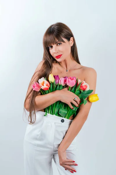 A slender girl presses flowers to her bare chest. Beautiful girl with a bouquet of tulips isolated on white background