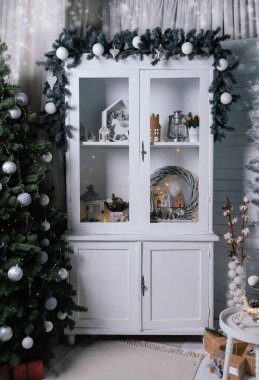Yeni yıl süslemeleri olan beyaz büfe. Dolapta yeni yıl oyuncakları, köknar ağacı ve çelenkler var. Stüdyo içi