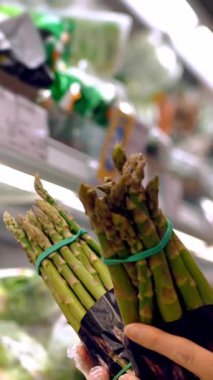 Asparagus officinalis. packaged asparagus, on shelves in a supermarket. a woman chooses asparagus to buy in a supermarket, in the grocery department, in the vegetable shop.