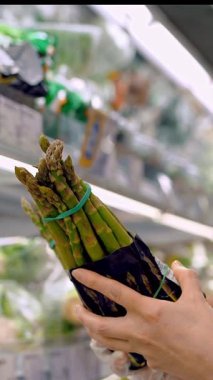 Asparagus officinalis. packaged asparagus, on shelves in a supermarket. a woman chooses asparagus to buy in a supermarket, in the grocery department, in the vegetable shop.