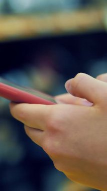 Süpermarkette cep telefonu. Markette akıllı telefon kullanmak. Yakın plan. Arka planda süpermarket raflarında telefonu olan eller. Birisi süpermarkette günlük yiyecek alışverişi yaparken akıllı telefon kullanıyor..