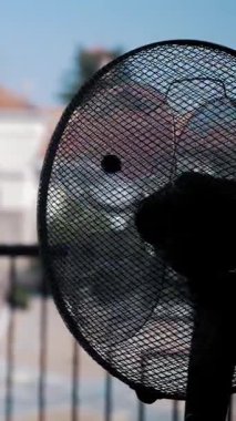 Elektrik vantilatörü. Elektrikli havalandırma. Yakın plan. Odada çalışan bir vantilatörün siyah silueti, pencerenin karşısında. Odayı soğutuyorum...