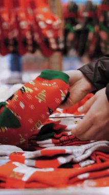 Noel hediyesi. Noel alışverişi, dekorasyon. Adil. Şenlik aksesuarları. Yakın plan. Kadın Noel hediyesi setini seçiyor, Noel Baba 'yla sıcak kırmızı çorapları, dükkanda. Mutlu Noeller ve mutlu yıllar. Alışveriş merkezi.