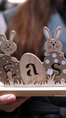 Paskalya indirimi. Yakın plan. Paskalya bayramında geleneksel paskalya tavşanları ve yumurtalarla süslenmiş ahşap bir süsleme tutan kadın elleri. Paskalya süslerinin alışverişi ve dükkandaki ev için hediyeler..