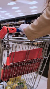 Bej ceketli uyanık bir müşteri, bir alışveriş arabasının sapına dezenfektan uygular, salgın hastalık ortamında bir süpermarkette sağlık güvenliğini vurgular.