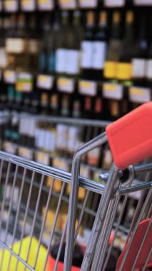 Şarap reyonunda süpermarket arabasını iten bir müşterinin el resmi. Alkol reyonundaki perakende alışveriş ve tüketici seçimini simgeliyor.