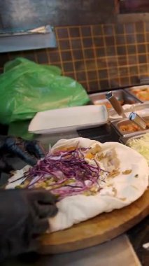 Şef şu malzemeleri kullanarak shawarma hazırlıyor: lavaş, et, sos, sebze, salatalık, soğan, lahana, baharatlı biber, patates, yeşillik, havuç