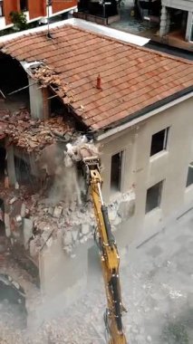 Şehir ortamındaki büyük bir kazıcı tarafından yıkılan yıkık dökük eski bir binanın ayrıntılı görünümü, yeniden yapılanma ve kentsel dönüşümü sembolize ediyor