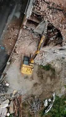 An excavator works amidst the debris and rubble, carefully tearing down an old, damaged building, paving the way for urban redevelopment in a bustling city area