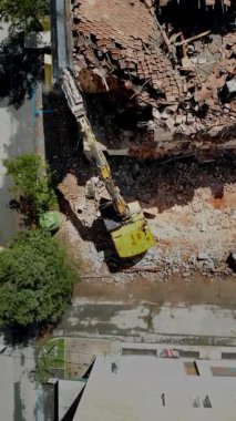 Şehir yıkım alanındaki molozların arasında, bozulmamış binalarla çevrili sarı bir kazıcının detaylı görüntüsü.