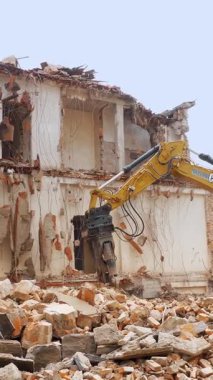 BIELLA, İtalya, 25 Nisan 2024: Parlak sarı bir kazıcı, çökmüş bir şehir binasının yıkılması sırasında, yenilenme ve kalkınmayı sembolize eden tuğla ve moloz yığınları arasında çalışır