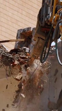 BIELLA, İtalya, 25 Nisan 2024: Hidrolik kol ve yıkım araçlarıyla donatılmış güçlü bir kazıcı, toz ve enkaz bulutu arasında etkin bir şehir binasını yıkıyor