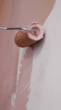 Duvar resmi. Su bazlı boya. Paten boyama. Onarım. Yakın plan. Boya silindiri kullanarak beyaz duvarı pembeye boyamak. Dairede, odada, evde, dairede tadilat yapıyor. Tamamlama ve inşaat işi