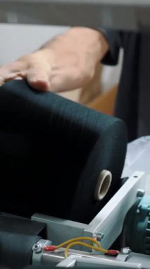 Bir işçi iplik makaraları taşır. Tekstil fabrikası ekipmanı. Tekstil fabrikası. Dönen yapım. İplik yapma süreci. Fabrika makineleri makaraları ya da pamuklu ya da yün ipliklerle bobinleri geri sarıyor.