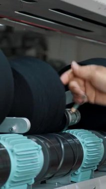 Bir işçi iplik makaraları taşır. Tekstil fabrikası ekipmanı. Tekstil fabrikası. Dönen yapım. İplik yapma süreci. Fabrika makineleri makaraları ya da pamuklu ya da yün ipliklerle bobinleri geri sarıyor.