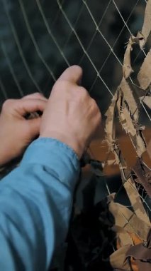 Kamuflaj ağı. Gönüllü. Yakın plan. Gönüllü asker ordunun askeri ihtiyaçları için yeşil ya da haki rengi kumaşlardan oluşan bir kamuflaj ağı örüyor. Ukrayna 'da savaş.