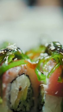 Suşi. Japon yemeği. Yemek pişirmek. Mutfak. Yakın plan. Suşi şefi susam tohumlarını serpiyor taze pişmiş suşi ruloları, siyah tabakta servis ediliyor. Sanat hizmeti. Asya yemekleri