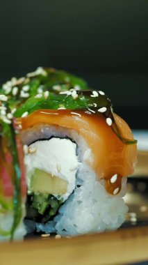 Suşi. Japon yemeği. Yakın plan. Siyah tabakta servis edilen taze pişmiş suşi ruloları dönüyor. Yemek pişirmek. Mutfak. Asya yemekleri