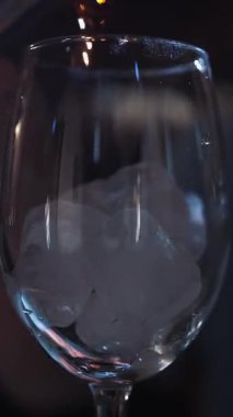 Kokteyl. Kokteyl yapıyorum. Yakın plan. Barmen, barın üstünde buzlu bir şarap bardağına beher kullanarak alkollü içecek doldurur. koyu arkaplan.