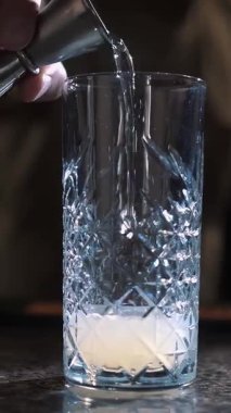 Kokteyl. Kokteyl yapıyorum. Yakın plan. Barmen bardağa alkollü içecek doldurur, beher kullanarak, tek eliyle, tezgahın üzerine. koyu arkaplan