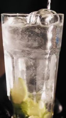 Kokteyl hazırlıyorum. Yakın plan. Barmen bütün malzemeleri ve buzları uzun bir kokteyl bardağıyla karıştırıyor..
