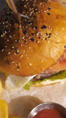 Hamburger yapıyorum. Yakın plan. Etli, sebzeli ve sahanda yumurtalı sulu burger. Patates kızartması ve domates sosuyla servis edilen hamburger. döndür.